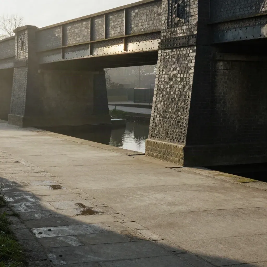 Misty West Midlands canal bridge, soot-dark brick and rail lines over calm stone towpath.